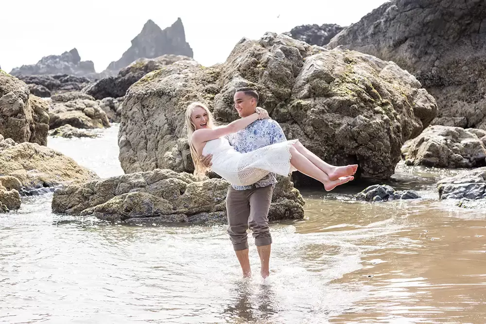 guy picks up his girl in the waves during the Cannon Beach Engagement Photos With Photographer Robert Knapp