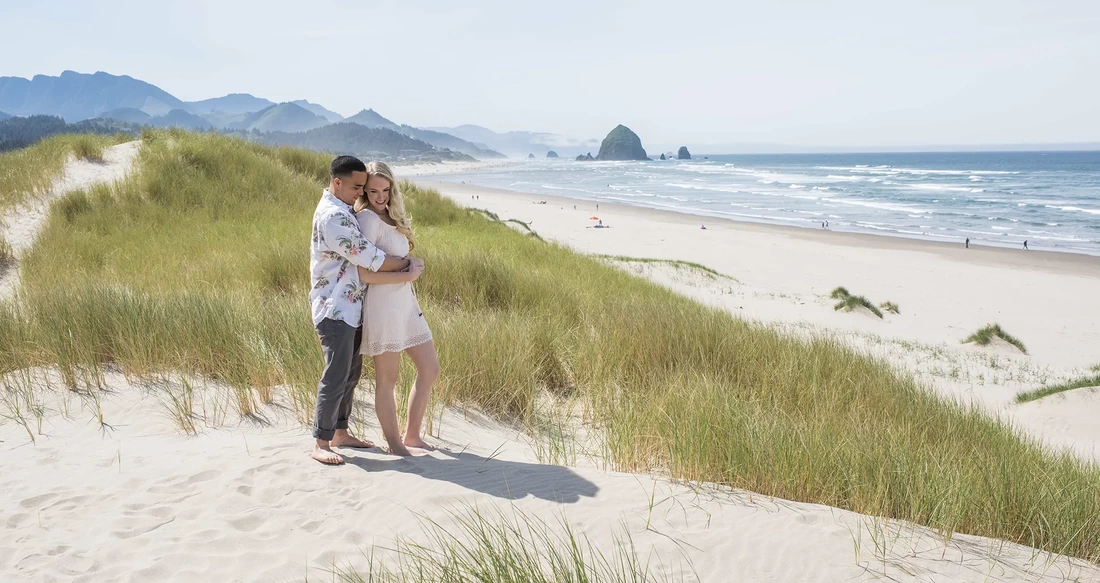 Cannon Beach Engagement Photos with photographer Robert Knapp. A couple stand in the sand overlooking the ocean and cannon beach against the horizon 