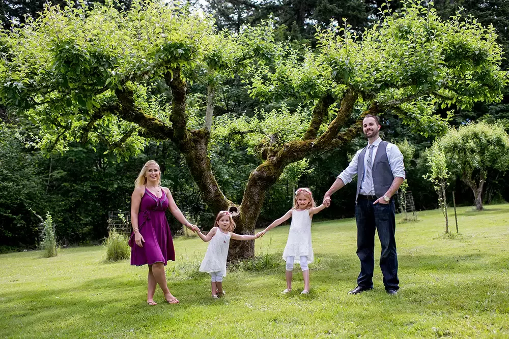 a family stands in front of an old apple tree Garden Photoshoot with Robert Knapp one of the highly sought after Family Photographers Portland has to offer