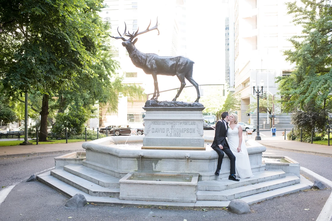 Hotel Deluxe Wedding in Portland Oregon by Photographer Robert Knapp the bride and groom look to kiss each other next to a bronze stag statue