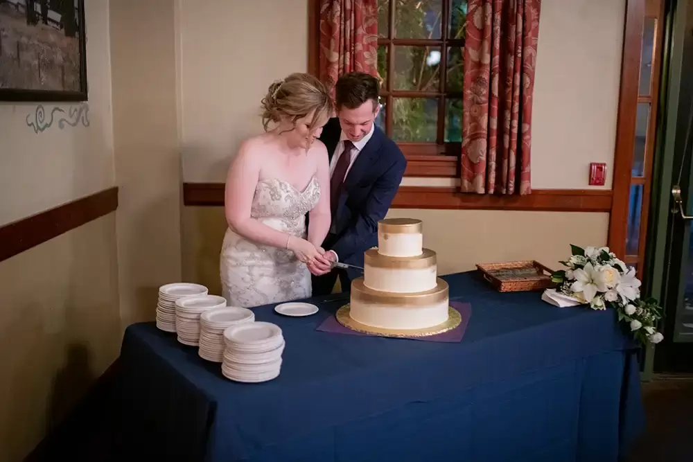 McMenamins Edgefield Weddings with Photographer Robert Knapp bride and groom cut the wedding cake. the cake is gold fade to white on each of the three tiers. There are maybe one hundred little plates ready to go. 