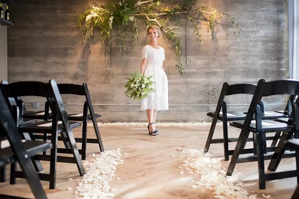 Oregon Wedding Photographers at Modern Art Photograph on location at opal 28 Bride standing at the ceremony location shot down the aisle, flower petals on the floor chairs for the reception empty