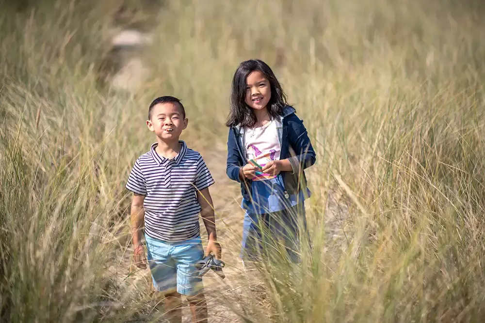 Two children walk on a path surrounded by grassy dunes together Portland ​Family Photographer Robert Knapp - Book Today! ​Family Photographer Robert Knapp in Portland - Book Today!