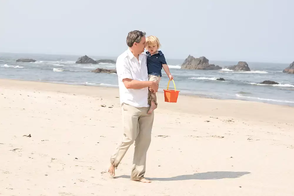 father and son walk together  on the beach their shadow is pointed toward the ocean   Family Pictures Beach Theme with Portland Family Photographer Robert Knapp