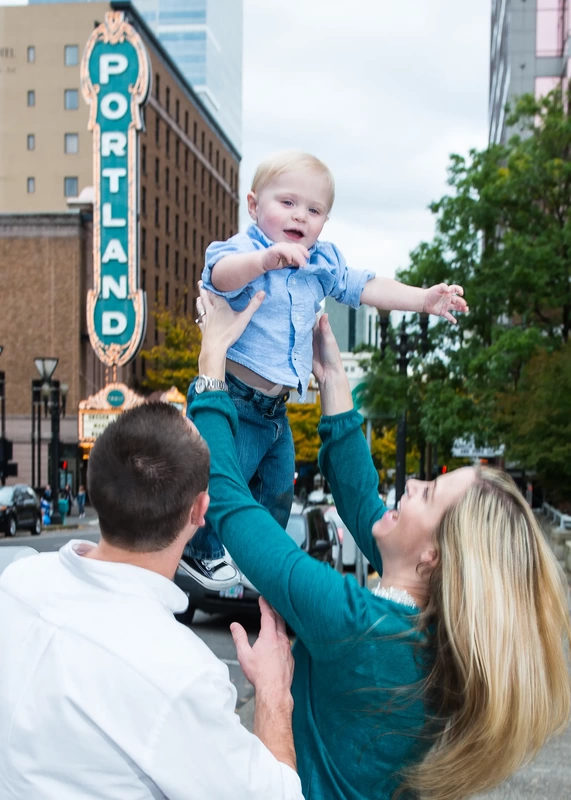 mother holds her baby up in the air in front of the portland marquee sign Family Photography by Robert Knapp in Portland City Parks